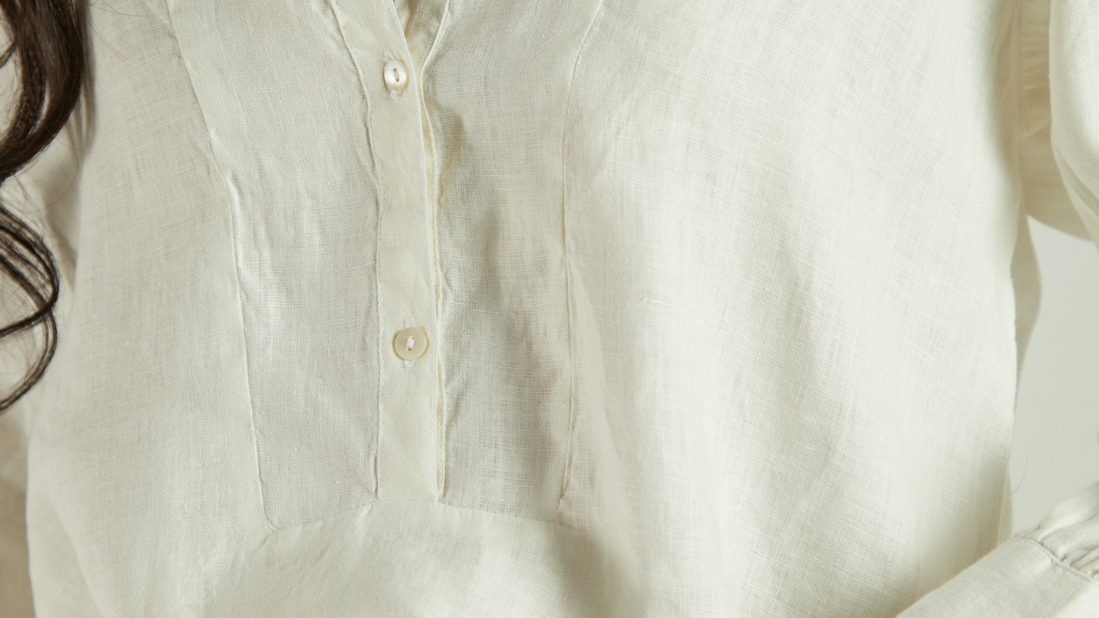 Detalhe de camisa clara em tecido leve, com botões e gola aberta; imagem ilustrativa de moda para o verão.