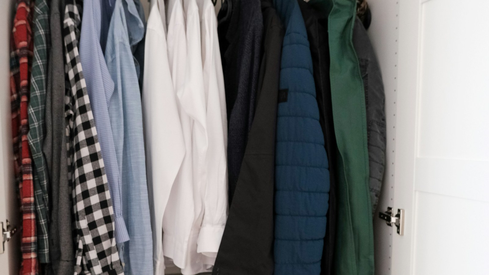 Roupas organizadas em cabides dentro de um armário; imagem ilustrativa de guarda-roupa cápsula.